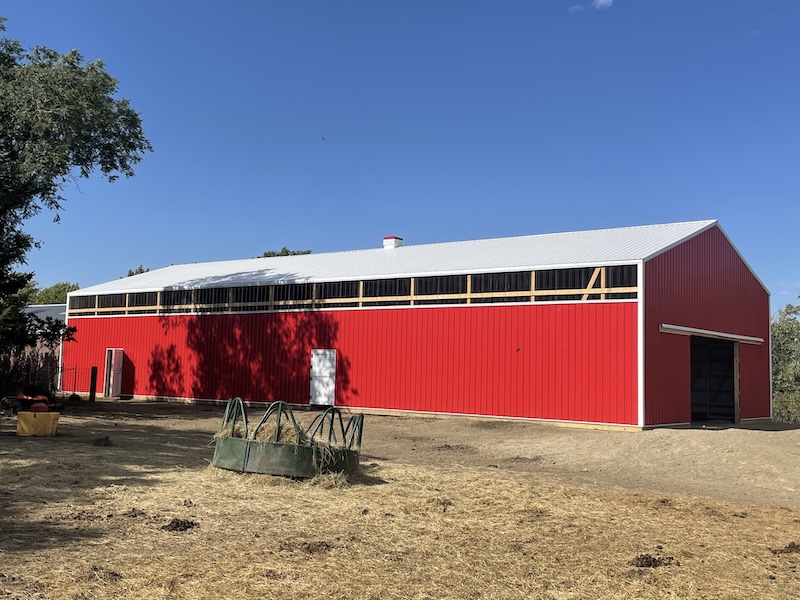 Picture of the indoor riding arena from the outside, a red barn-like structure