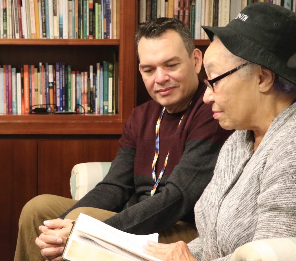 Two people sit in front of a bookcase looking at an open book
