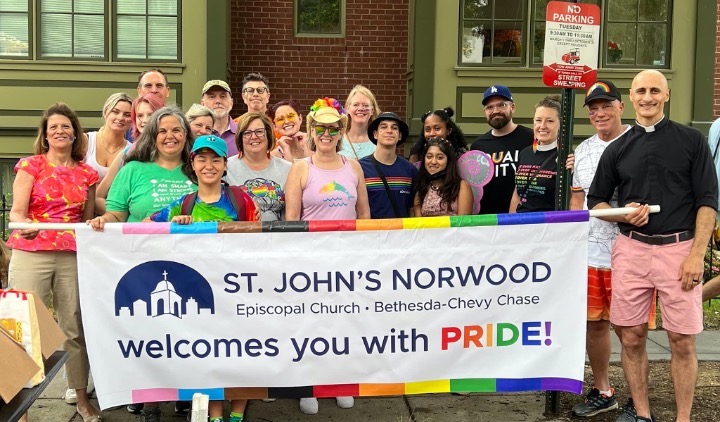 A group of young adults gathers behind a parade banner that says, "St. John's Norwood Episcopal Church, Bethesda-Chevy Chase, welcomes you with PRIDE!