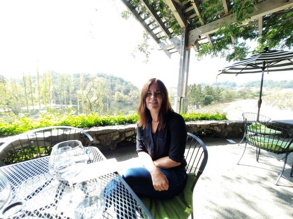 Amanda Szakats sits on an outdoor patio overlooking a wooded landscape.