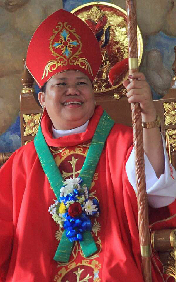 Bishop Dacuycuy smiles, wearing a red bishop's mitre and holding her crozier.