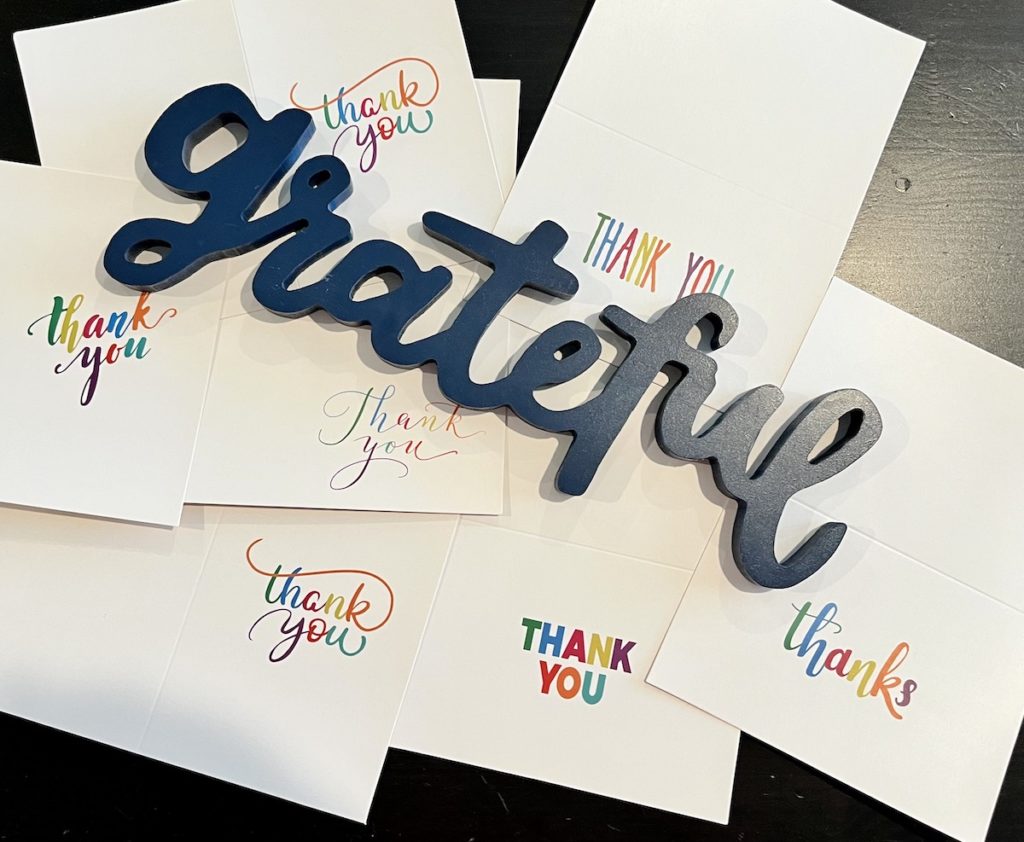 Blue wooden "Grateful" cutout lying on several "Thank You" cards